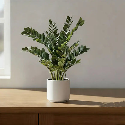 Artificial plant in a white pot on a wooden surface.