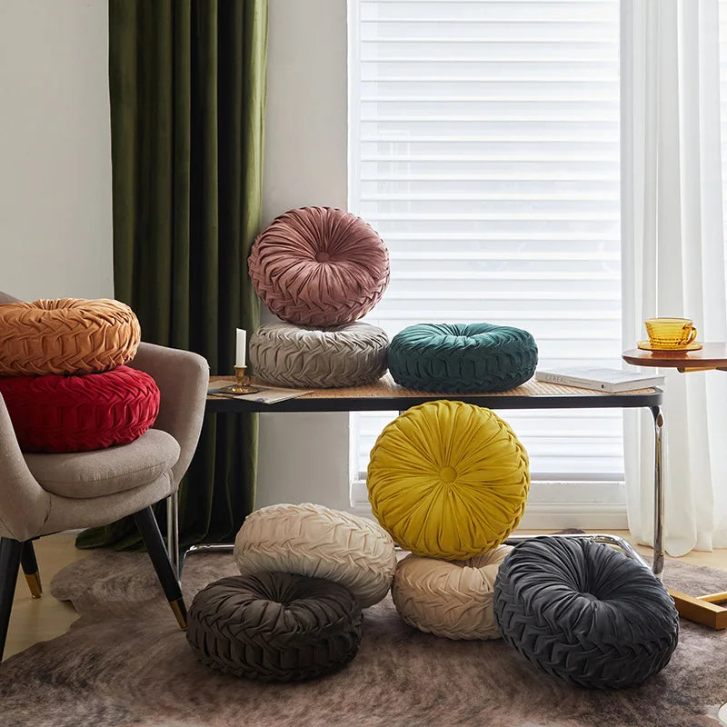 Colorful round pillows on a table and floor in a room with curtains and a window.