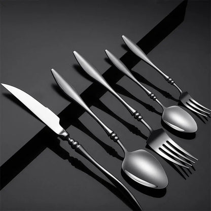 A set of six dark silver utensils on a black surface.