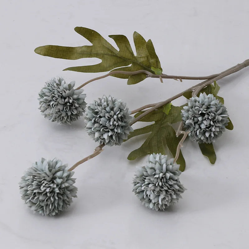 A single stem of artificial pale blue dahlia flowers with green leaves.