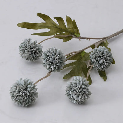 A single stem of artificial pale blue dahlia flowers with green leaves.
