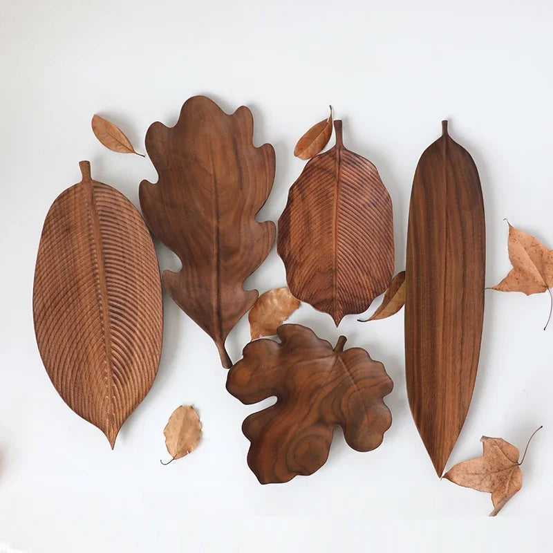 A flat lay of five different dark wood leaf-shaped serving platters and small dried leaves on a white background.