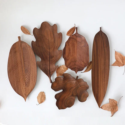 A flat lay of five different dark wood leaf-shaped serving platters and small dried leaves on a white background.