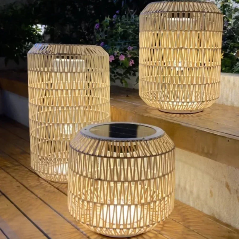 Three woven outdoor lanterns on a wooden deck with plants in the background