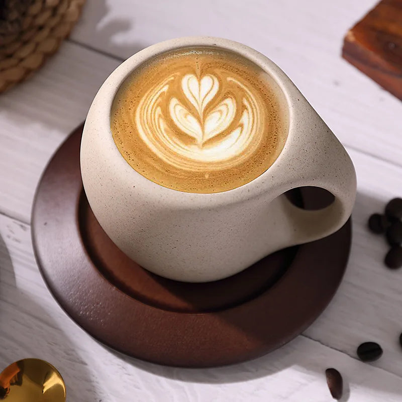 A rustic coffee cup with latte art, on a wooden saucer.