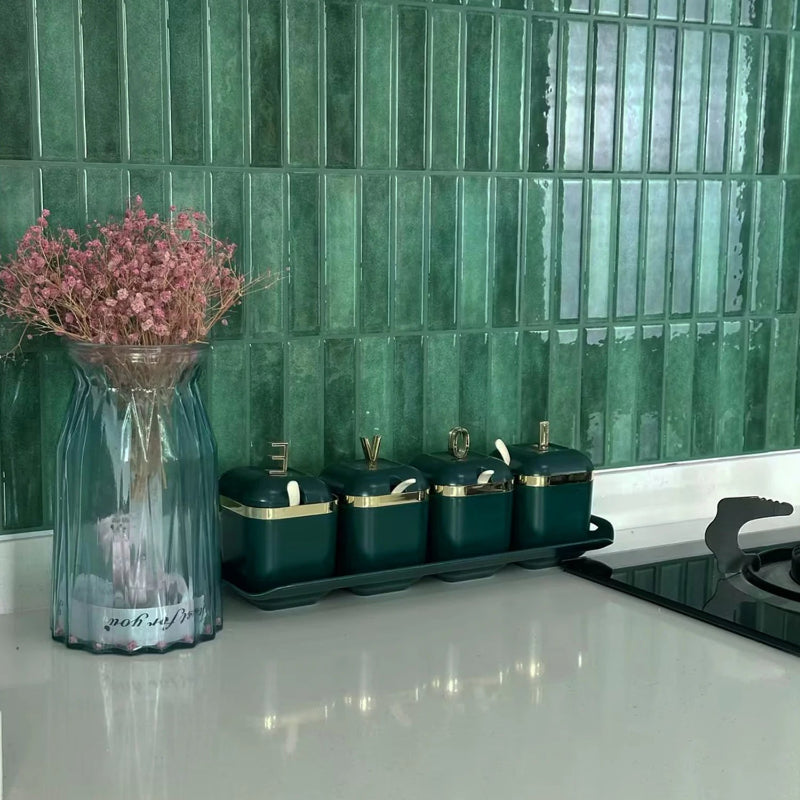 Kitchen counter with green rectangular tiles and a vase of pink flowers.
