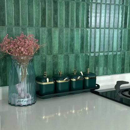 Kitchen counter with green rectangular tiles and a vase of pink flowers.