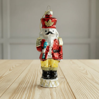 Decorative glass nutcracker ornament with red hat and outfit on a white background