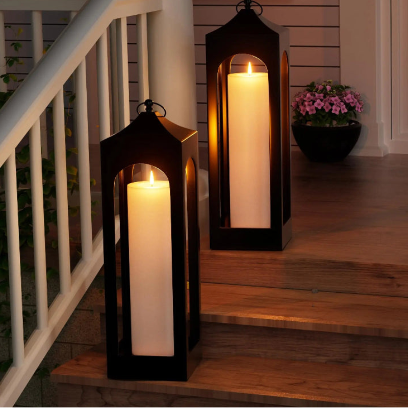 Two flameless pillar candles in black lanterns illuminate wooden steps at night.