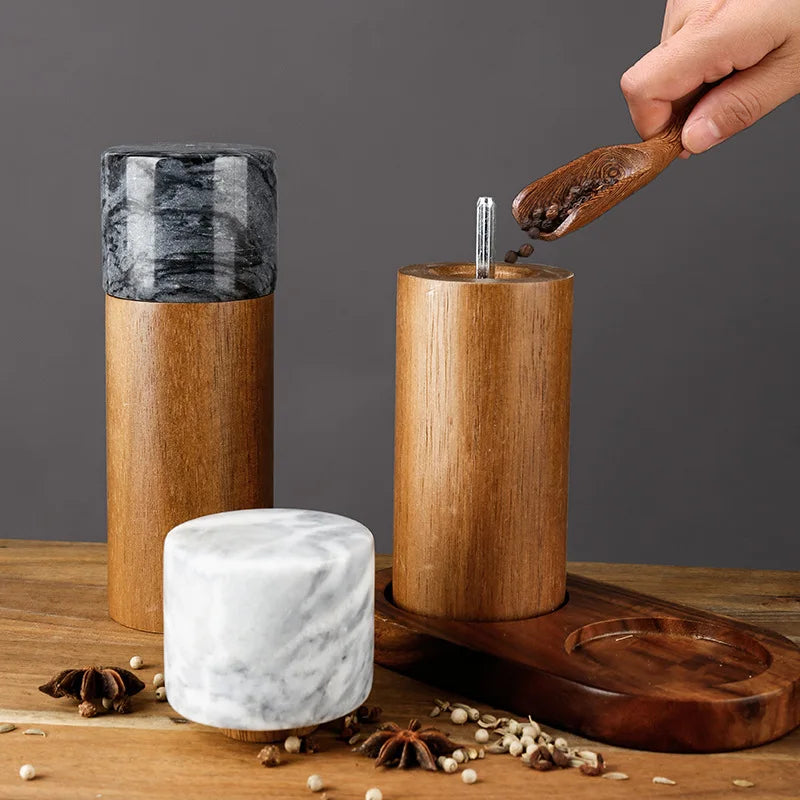 A hand refilling a wooden spice grinder with peppercorns.