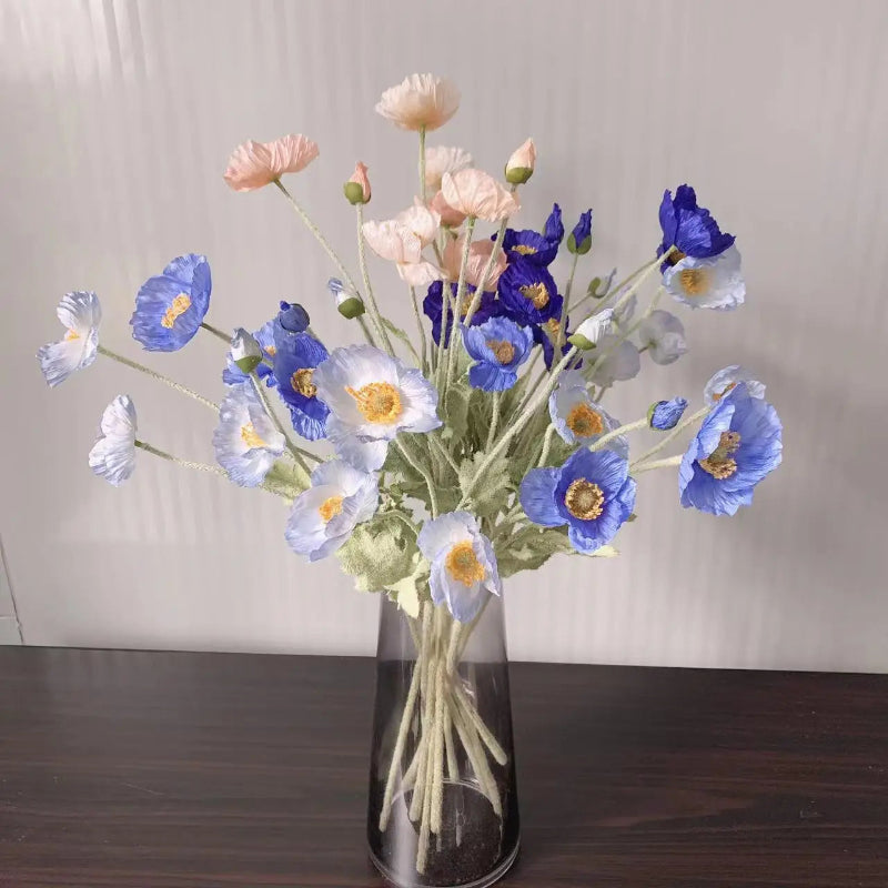 A clear vase holds a bouquet of pink, blue, and white poppies.