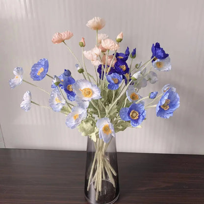 A clear vase holds a bouquet of pink, blue, and white poppies.