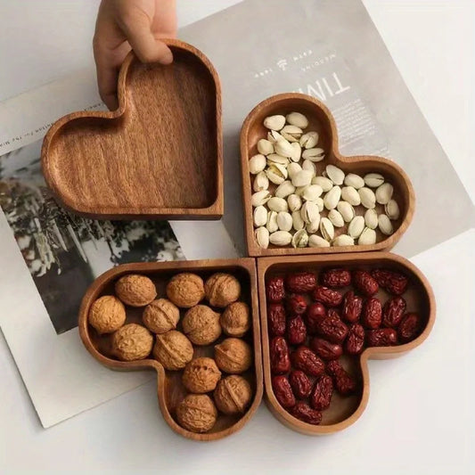 Four heart-shaped wooden bowls arranged to form a clover, filled with pistachios, walnuts, and dried dates, with one empty bowl being held.
