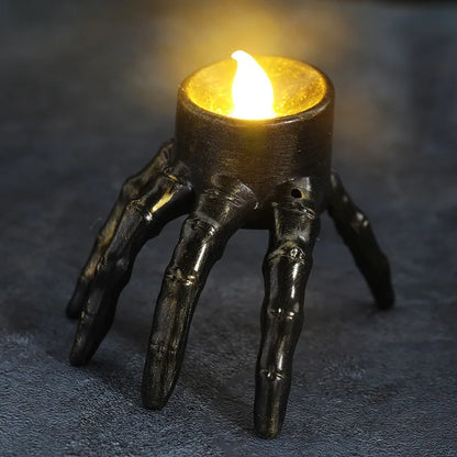 A lit candle in a holder shaped like a skeletal hand.