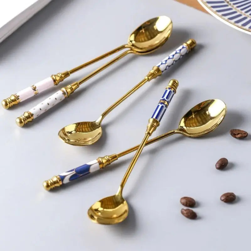 Set of decorative spoons with gold handles and ceramic handles on a white surface with coffee beans.