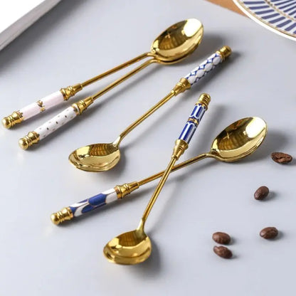 Set of decorative spoons with gold handles and ceramic handles on a white surface with coffee beans.