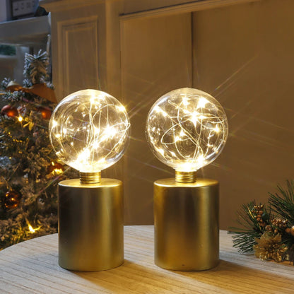 A pair of modern table lamps with gold cylindrical bases and clear glass globe shades filled with warm white fairy lights.