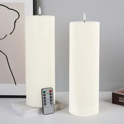 Two white flameless pillar candles, one with a remote, sit on a surface with minimalist decor.