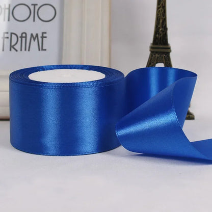 Blue satin ribbon roll with a small section unrolled on a neutral background