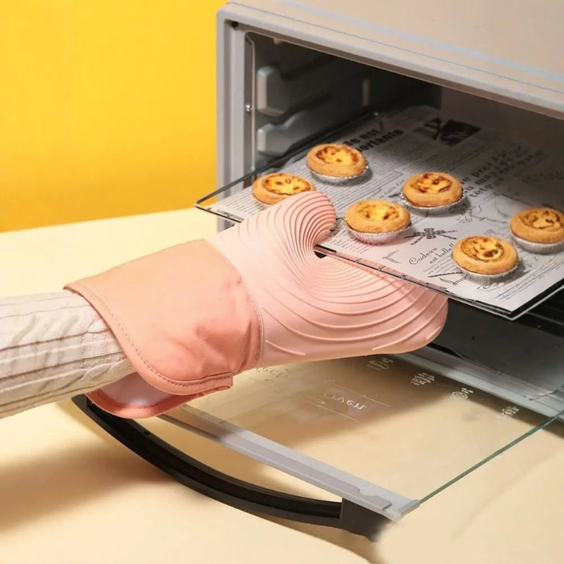 Person wearing a pink oven mitt removing a tray of baked goods from an open toaster oven.