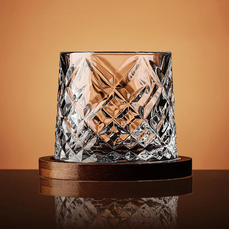 An empty, cut-crystal whiskey glass with a diamond pattern sits on a wooden coaster.