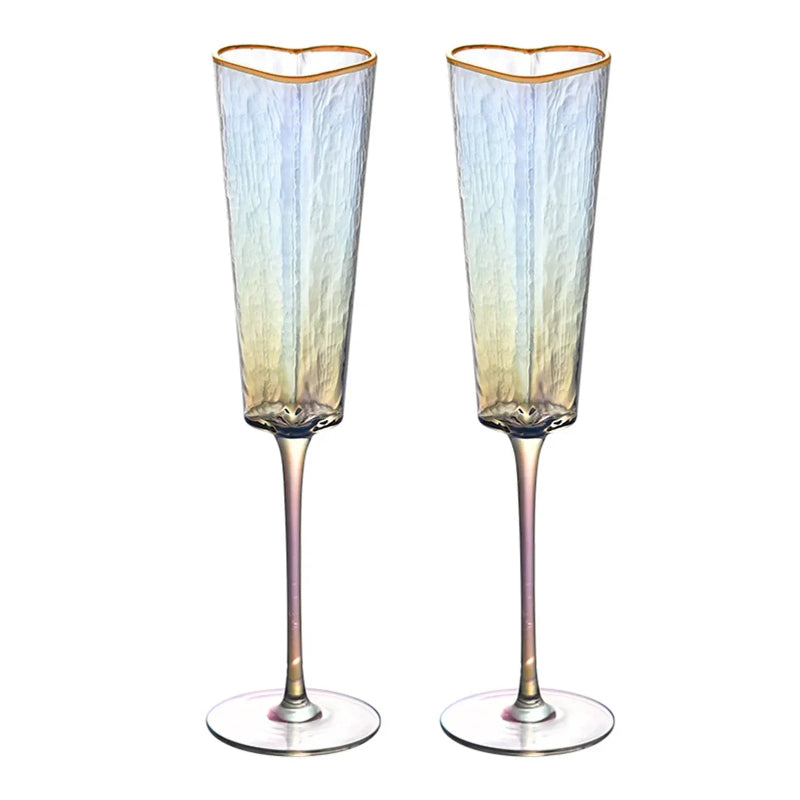 Two empty, iridescent, heart-shaped champagne flutes with gold rims, isolated on a white background.