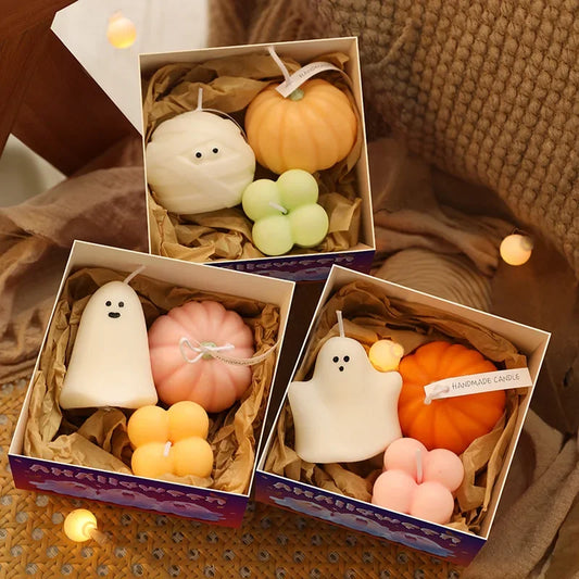 Three boxes display Halloween-themed candles. The top box contains a white ghost-shaped candle, a pumpkin-shaped candle, and a four-leaf clover-shaped candle. The middle box features a white ghost-shaped candle, a pink pumpkin-shaped candle, and two stacked orange cube-shaped candles. The bottom box includes a white ghost-shaped candle, an orange pumpkin-shaped candle, and a pink flower-shaped candle.