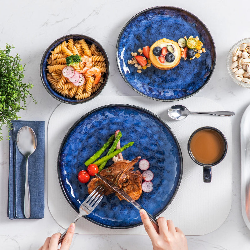 A vibrant blue dinnerware set holds a full meal, including meat, pasta, and a fruit tart.