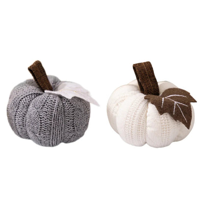 Two knitted pumpkins, one gray and one white, each with a brown stem and a fabric leaf, isolated on a white background.