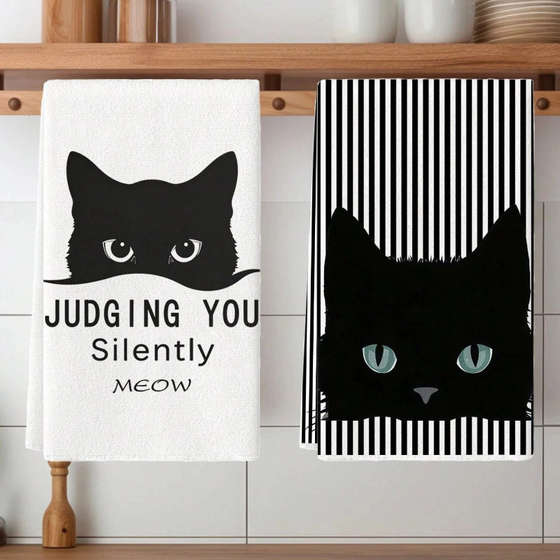 Two cat-themed towels on a wooden shelf with kitchen items in the background.