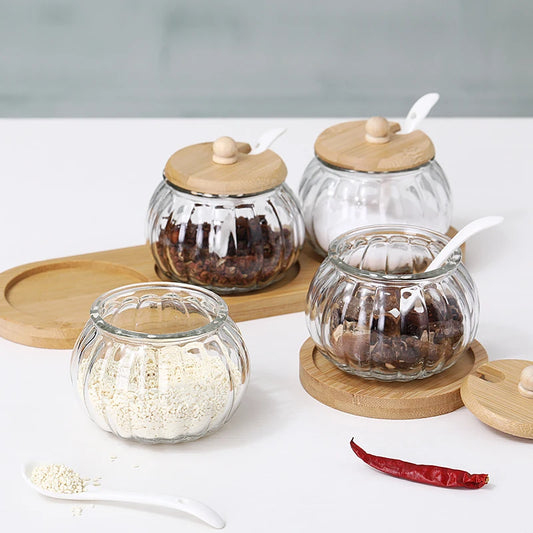 Four pumpkin-shaped glass jars with wooden lids and spoons, on a bamboo tray.