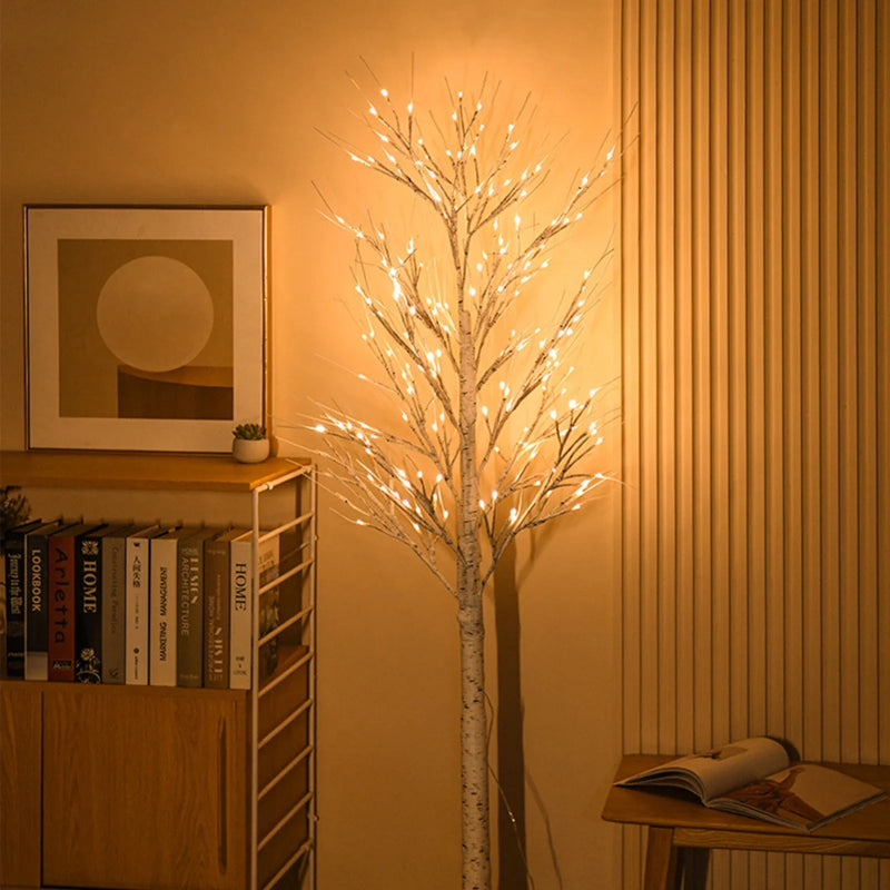 Decorative light tree in a room with books and a painting on a shelf.