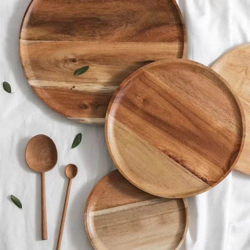 Three round wooden plates and two wooden spoons on a white cloth, with a few green leaves scattered around.