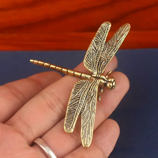 Gold dragonfly-shaped object held in a hand with a colorful background