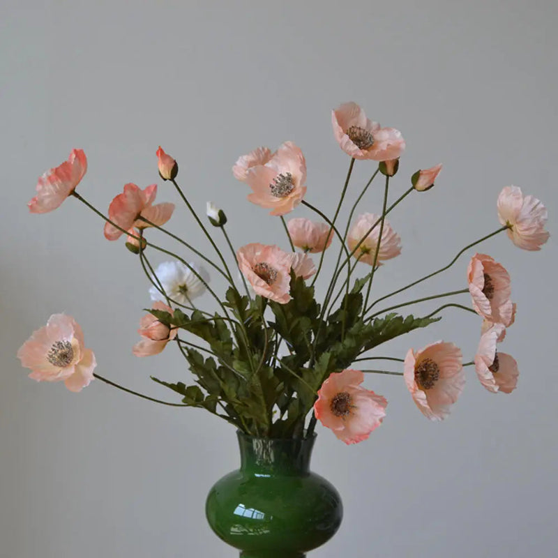 A dark green vase holds a bouquet of light pink poppies.