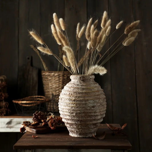 Rustic, textured terracotta vase with dried bunny tail grass on a dark wooden table.