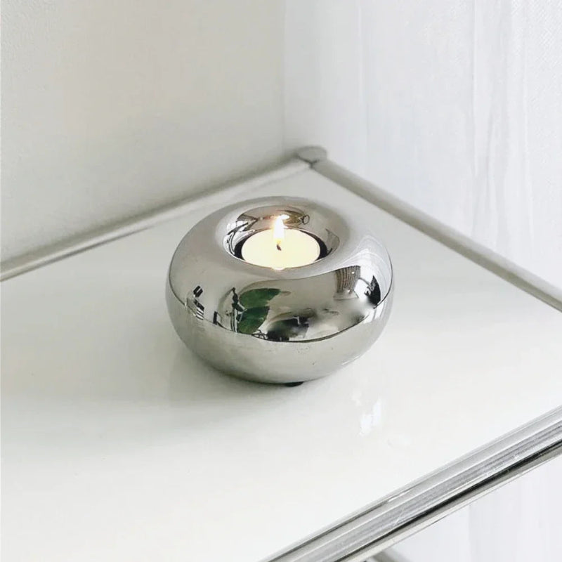 Silver candle holder with a lit candle on a white surface