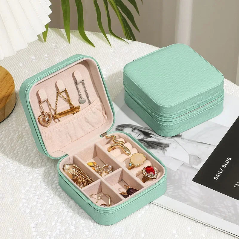 Two light green, square, zippered jewelry boxes, one open to reveal various rings and earrings neatly stored in compartments.