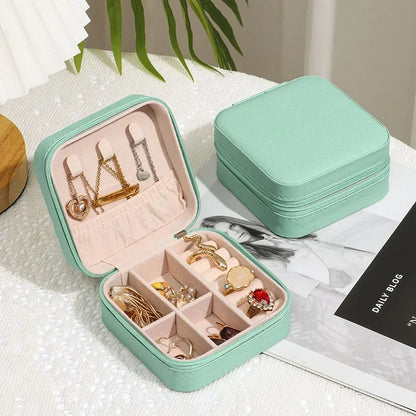 Two light green, square, zippered jewelry boxes, one open to reveal various rings and earrings neatly stored in compartments.