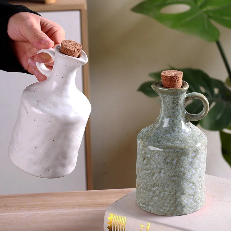Two ceramic oil bottles with cork stoppers on a wooden surface.