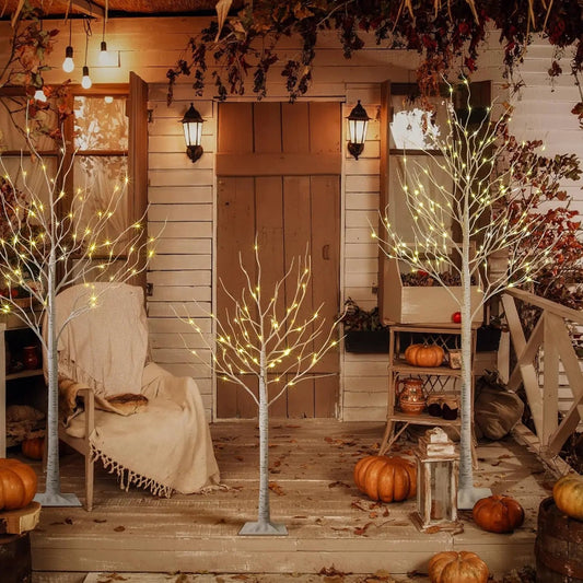 Decorative outdoor setting with lit trees, pumpkins, and a cozy chair on a wooden deck.