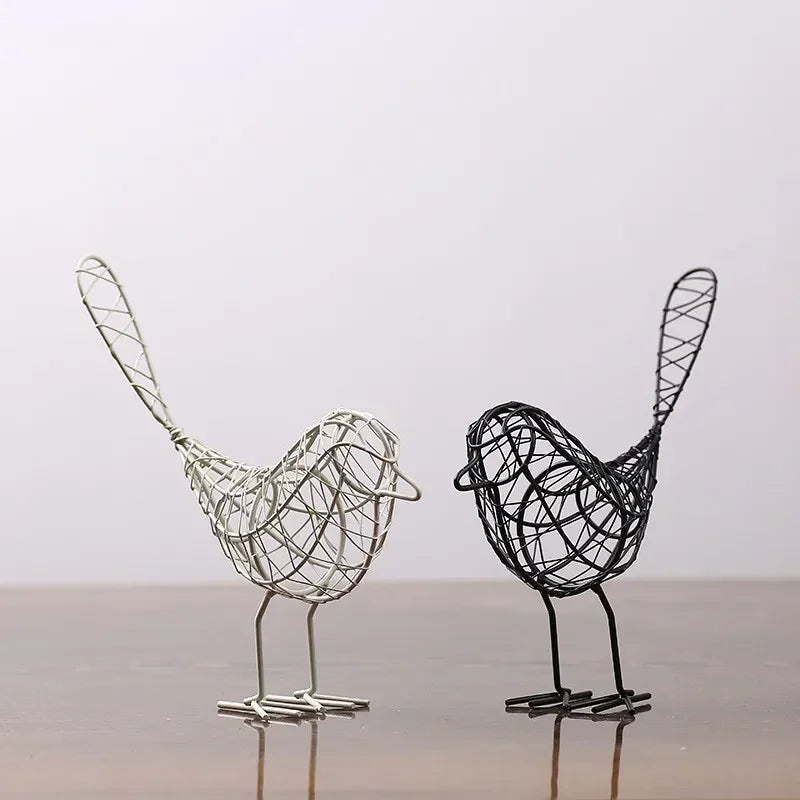 Two wire bird sculptures, one silver and one black, on a reflective surface with a light gray background.