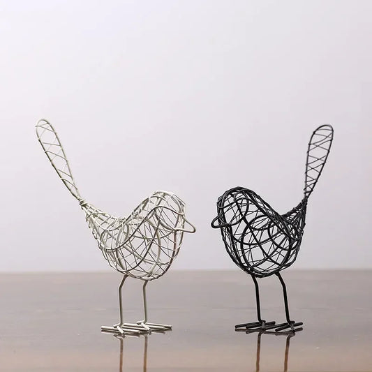 Two wire bird sculptures, one silver and one black, on a reflective surface with a light gray background.