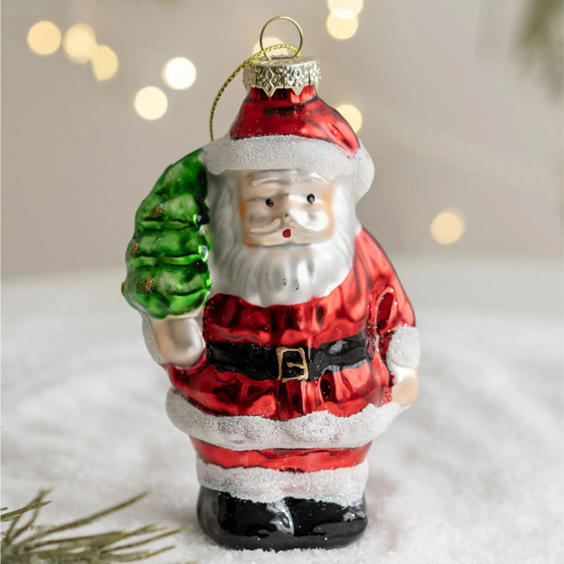 Glass ornament of Santa Claus holding a green tree against a blurred light background