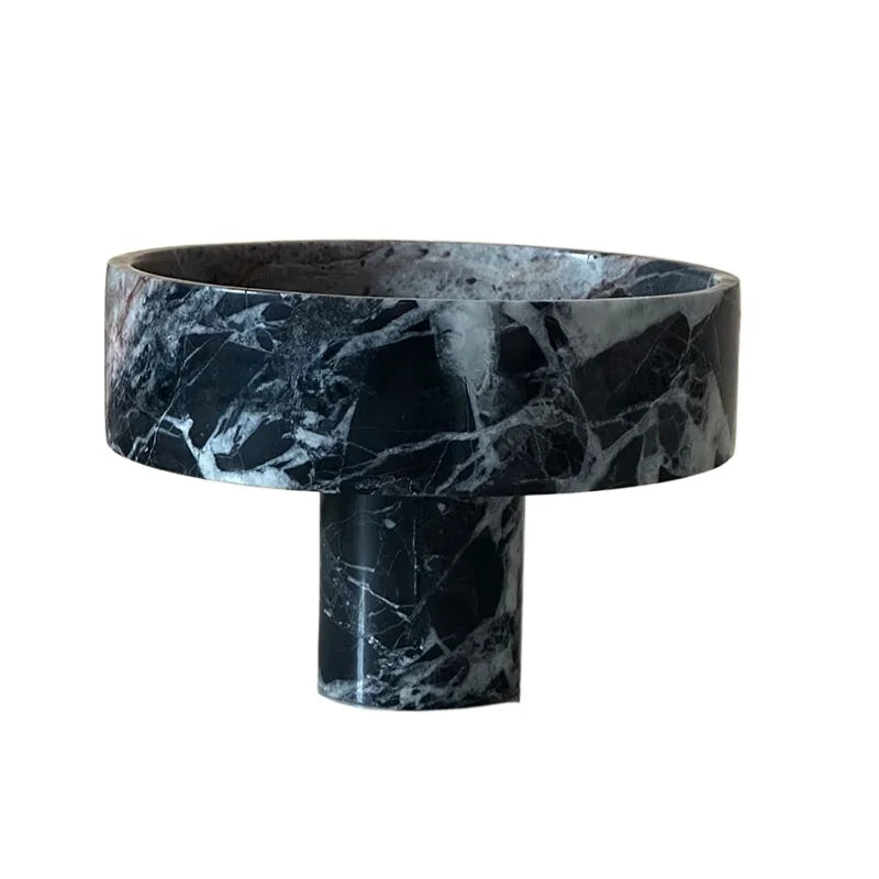 A round marble vessel with a black and white marbled pattern stands on a cylindrical pedestal, offering a modern twist. The sleek design features smooth, polished surfaces, making it an ideal premium fruit bowl for contemporary decor.