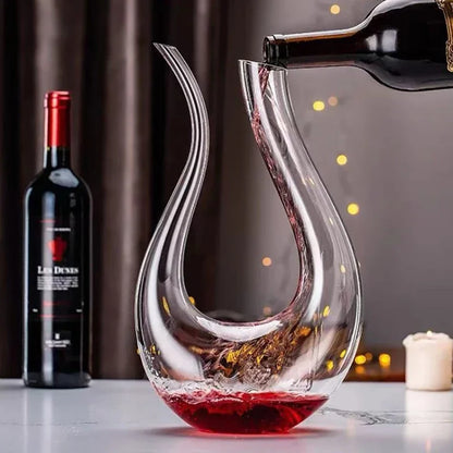 A bottle of red wine pouring into a uniquely shaped glass decanter.