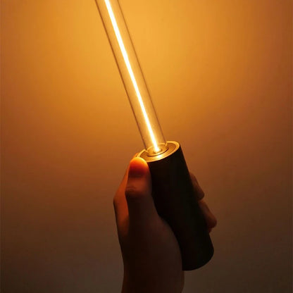 A hand holding a black cylindrical lamp with a glowing gold tube.