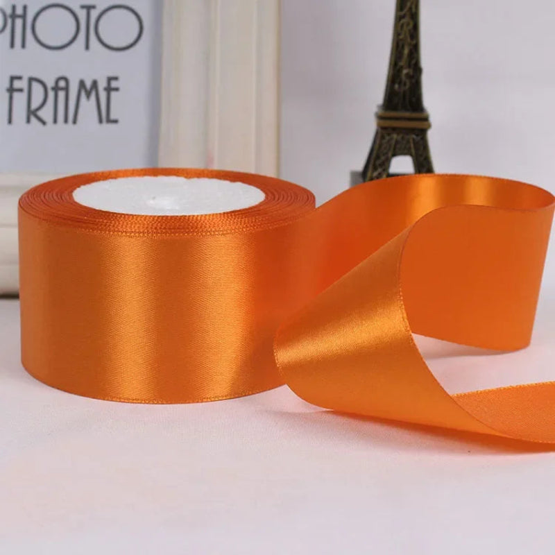 Orange satin ribbon with a spool on a light background