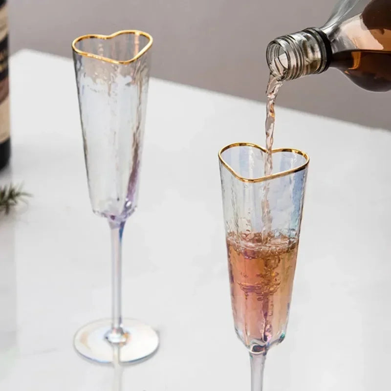 A hand pouring liquid from a bottle into a heart-shaped champagne flute.