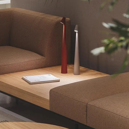 Two minimalist cone-shaped lamps, red and white, on a wooden coffee table between couches.